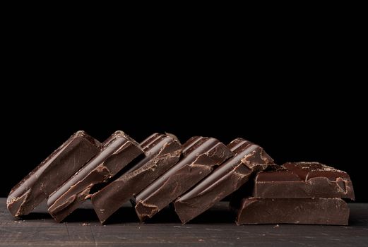 broken black chocolate on a wooden table, culinary sweet ingredient, close up, copy space