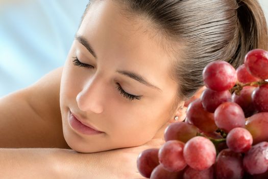 Close up portrait of attractive young woman relaxing with eyes closed in spa.Out of focus bunch of grapes in foreground.