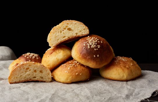 baked round bun with sesame seeds, black background, home baking, close up