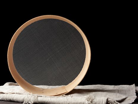 round wooden sieve on a black background, outdated kitchen utensils, copy space