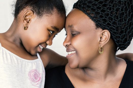 Close up face shot of african mother and daughter looking at each other. Tender close up portrait of kid going head with mother isolated against white background.
