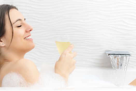 Close up portrait of attractive young woman enjoying champagne in foam bath.