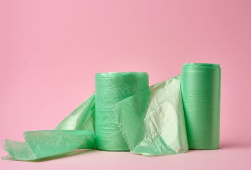 two rolls green plastic bags for trash bin on pink background, close up