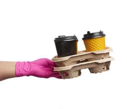 hand in a pink latex glove holds a paper tray with disposable cardboard cups and plastic covers on a white background, safe and contactless delivery of on-line orders during epidemics