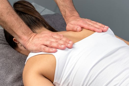 Close up detail of therapist applying pressure with hands on female shoulder.