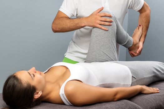 Close up of male osteopath doing leg and knee treatment on female patient.