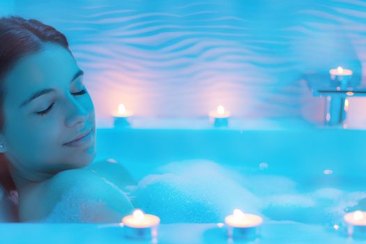 Close up  Low light ambient portrait of woman enjoying foam bath.Blue ambient with decorative candles along bath tub.