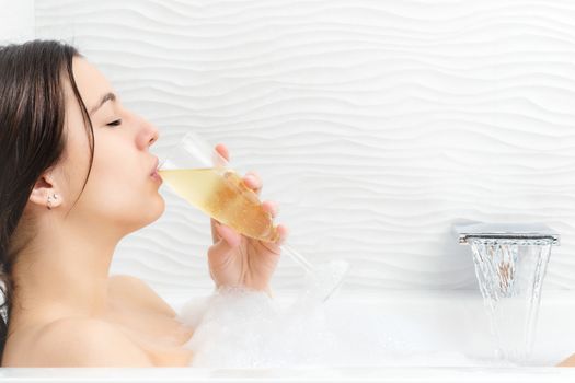 Close up portrait of young woman relaxing in foam bath drinking champagne.
