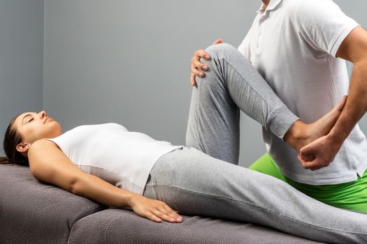 Close up of male physiotherapist doing manipulative leg treatment on young woman.