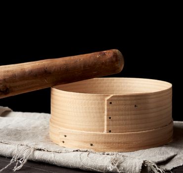 round wooden sieve rolling pin on a black background, outdated kitchen utensils