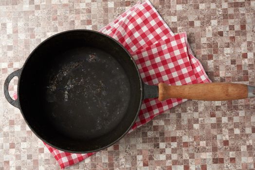 empty black round frying pan with wooden handle, brown table, top view