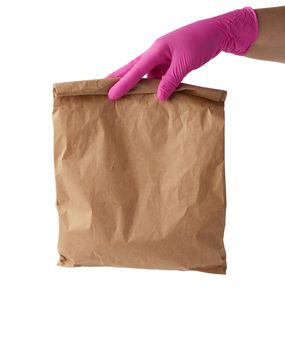 hand in a pink latex glove holds a full paper bag of brown craft paper, concept of remote and contactless food delivery, safe receipt of orders, white background