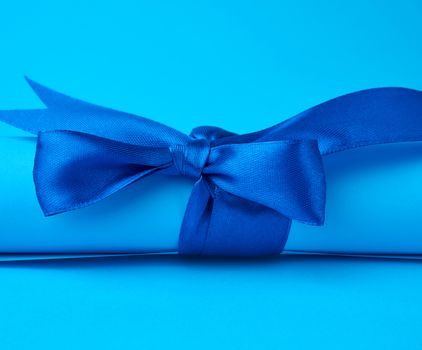 roll of blue paper tied with a silk blue ribbon, blue background, close up