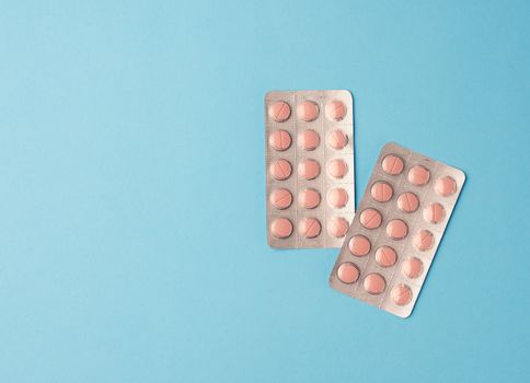 round pink pills in blister packs on a blue background, copy space