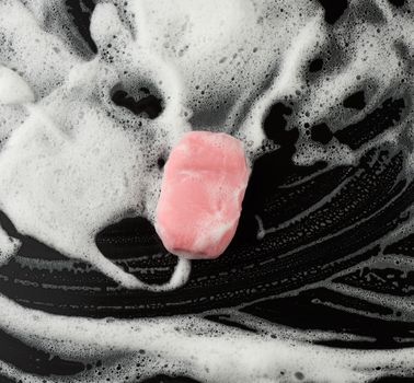 white soap foam and pink soap on a black background, top view, concept of cleanliness, antibacterial, close up