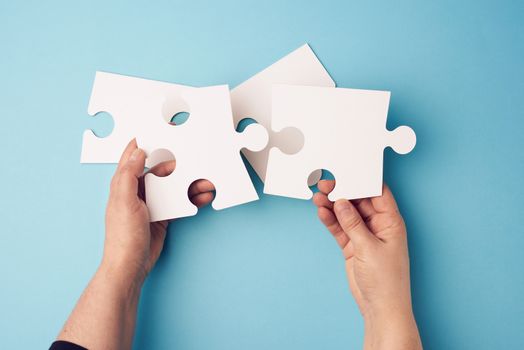 two female hands holding big paper white blank puzzles on a blue background, concept of business