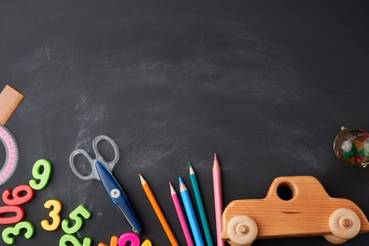 wooden multi-colored pencils, plastic numbers, scissors, wooden toy car on a black background, concept back to school, copy space