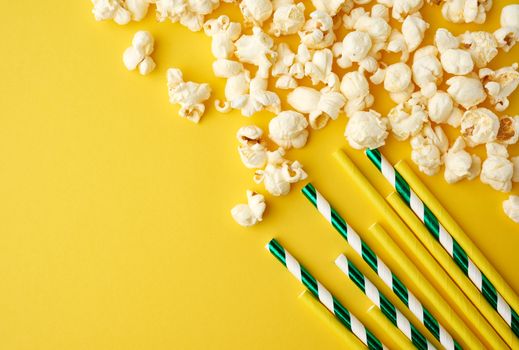white delicious popcorn and paper tubes for cocktail on a yellow background, place for an inscription, snack while relaxing, flat lay