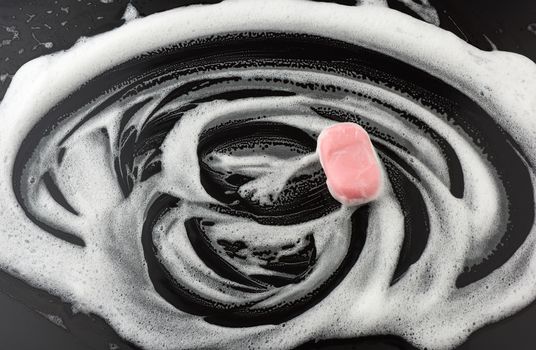 white soap foam and pink soap on a black background, top view, concept of cleanliness, antibacterial