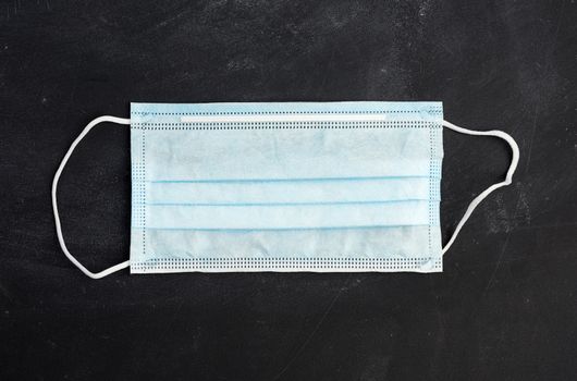 blue disposable medical mask for protection against the virus on a black chalk board, top view