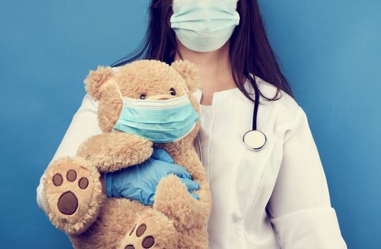 woman doctor pediatrician holds brown teddy bear in hand in white medical disposable mask, concept of preventing epidemics and pandemics against flu