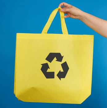 woman's hand holds a yellow viscose ecology bag, recyclable material, blue background