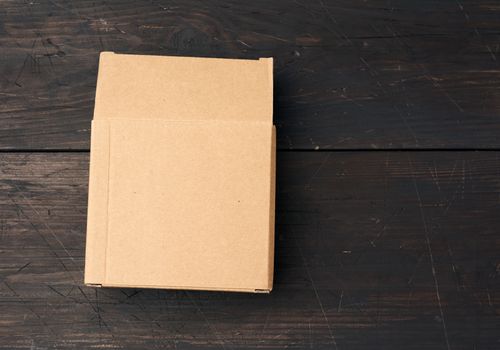 brown square cardboard box for transporting goods on brown wooden background. Packaging design, top view, copy space