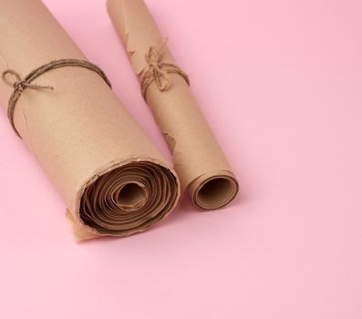 twisted rolls of brown paper on a pink background, close up