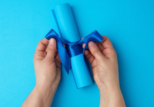 roll of blue paper tied with a silk blue ribbon, blue background, copy space