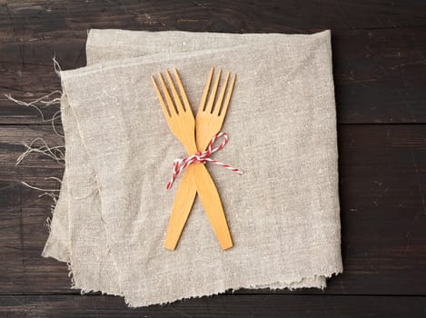 two wooden forks are tied with a rope and lie on a brown wooden background from boards, top view