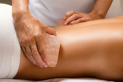Close up detail of himalayan salt stone massage. Therapist massaging lower back of woman with hot salt brick.
