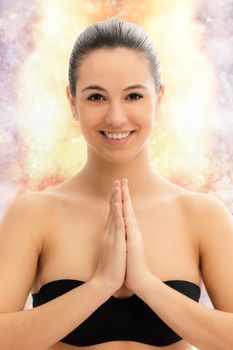Close up conceptual portrait of young woman meditating with hands together against colorful background.