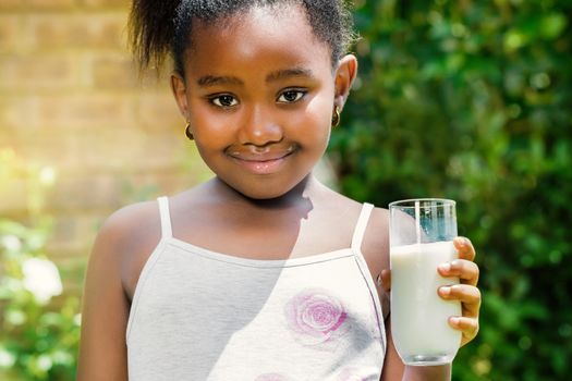 Close up portrait of cute little african girl holding glass with milk in garden.