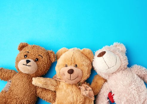 various teddy bears lie on a blue background head to head and look up, concept of friendship and mutual assistance, copy space