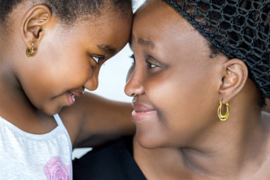 Close up face shot of african mother and little daughter joining heads. Mother and child showing affection isolated on white background.