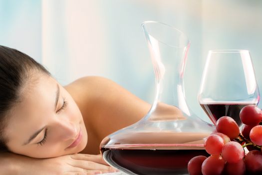 Close up portrait of red wine decanter and bunch of grapes with woman in background.Young girl laying in wine spa.