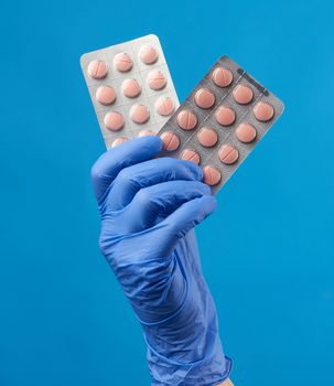 female hand in a blue sterile rubber glove holds a stack of pills in a blister pack on a blue background