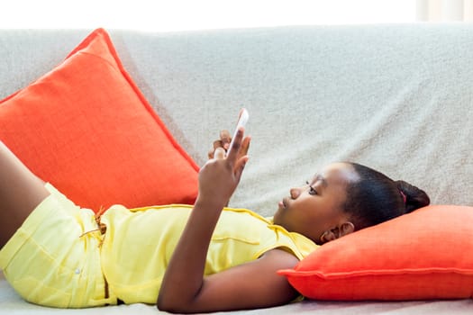 Close up portrait of cute little african girl with ponytail laying on couch at home. Kid looking at movie on digital tablet.