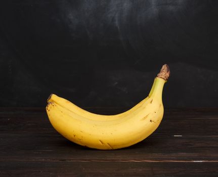bunch of yellow unpeeled ripe bananas on a brown wooden table, black background