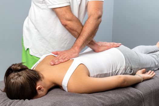 Close up of male osteopath doing manipulative physical treatment on female spine.