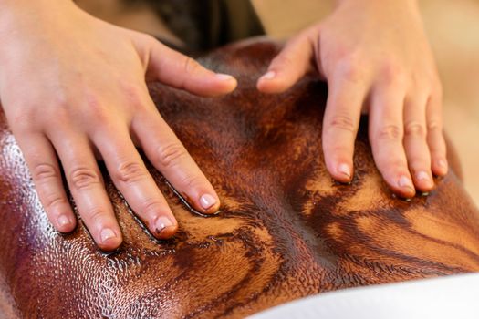 Close up of hands doing antioxidant cacao massage on female back. 
