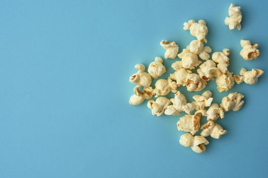 white delicious popcorn on a blue background, place for an inscription, snack while relaxing and watching a movie, top view