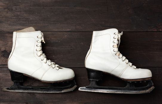 pair of white leather skates for figure skating on a brown wooden background, sports equipment, top view