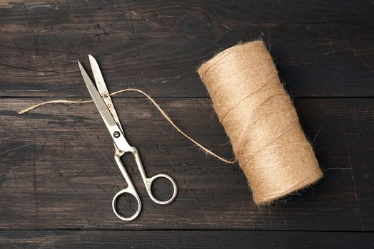 brown thread twisted into a spool and vintage metal scissors on a wooden background from boards, top view