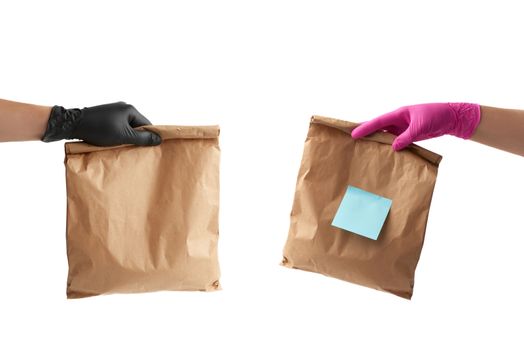 hand in a black and pink latex glove holds a full paper bag of brown craft paper, the concept of remote and contactless food delivery, safe receipt of orders, white background