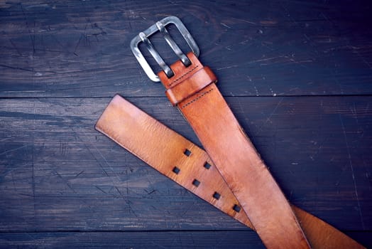 brown leather men's belt with metal buckle on a wooden background, top view