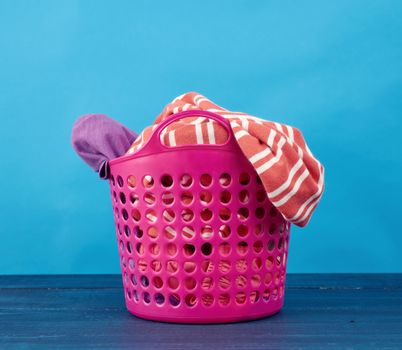 full of dirty clothes plastic pink basket in the hole for collecting laundry, container on a blue background