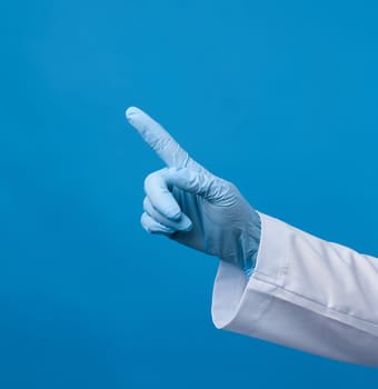 medic woman in white coat, wearing in blue sterile gloves, showing hand gesture indicating the subject, blue background