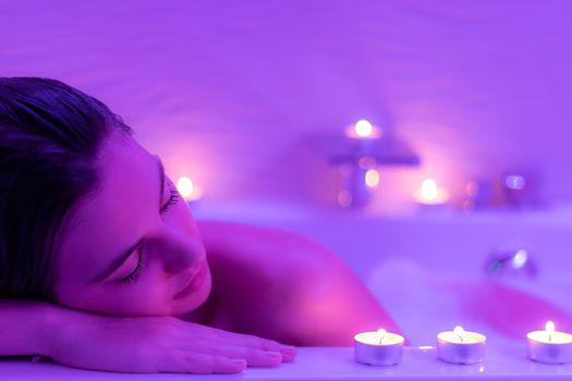 Close up Low light portrait of young woman relaxing in foam bath.Low colorful candlelight ambient with candles on bath tub.