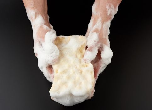 two female hands in white soapy foam hold a wet sponge and wipe the black surface, concept of cleaning and washing surfaces, top view